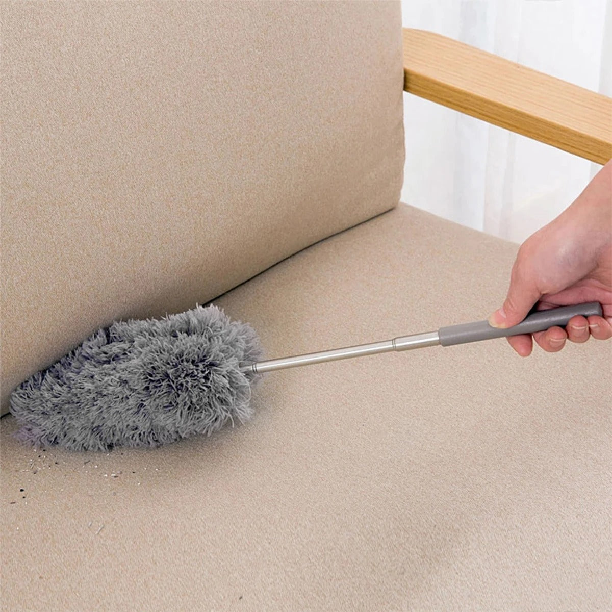 Person cleaning a beige sofa with a duster tool.