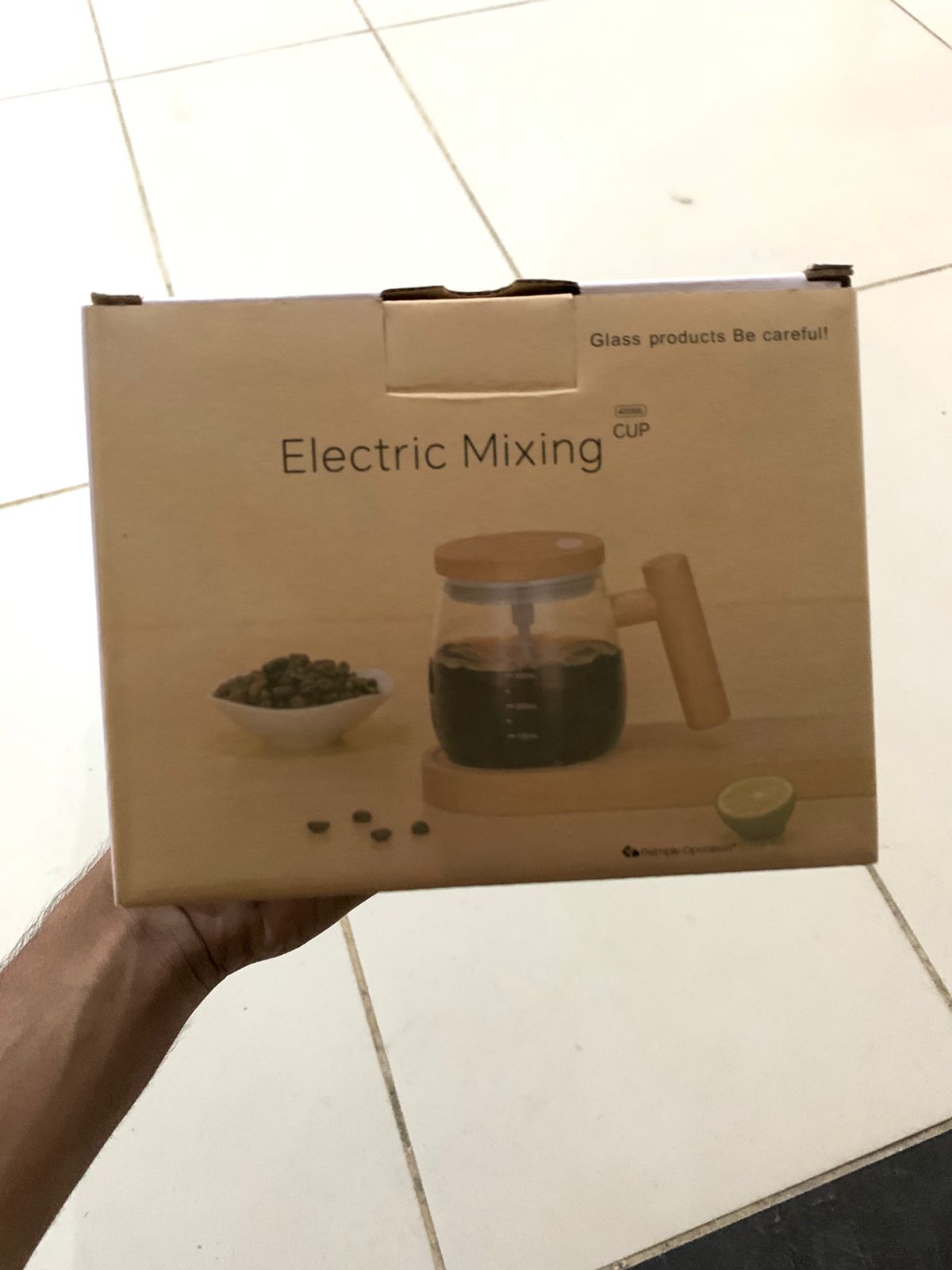Box of an electric mixing cup with a glass product on a tiled floor.
