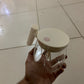 Clear glass jar with a white lid and handle held by a hand on a tiled floor.